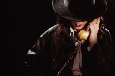 Dark noir portrait of a female detective holding a retro telephone receiver. Private detective, spy, investigation concept