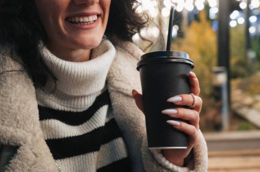 Siyah bir kahve fincanından kadınların ellerini bir kış kenti sokağının arka planına yakın çekim. Şehir yürüyüşünün Noel atmosferi.