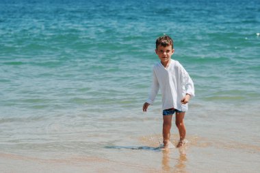 Sert sularda sahilde bir yaz tatili oynayan mutlu çocuk.