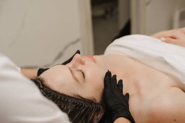 Bir kadın kozmetik uzmanının yakın plan fotoğrafları müşterilere yüz derisi masajı yapıyor. Kozmetik prosedür kavramı