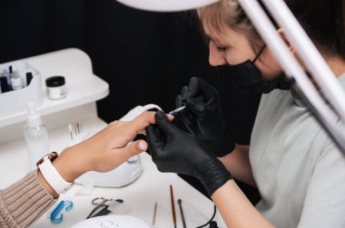 Manikür servisi. Yakın plan. Tırnak cilası sürüyorum, yüzeyi düzleştiriyorum. Manikürcü onun tırnaklarını şeffaf bir jel cilasıyla boyuyor. İyi bakımlı tırnaklar. Profesyonel salon el bakımı.