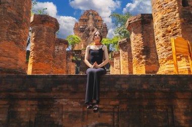 A female tourist sit on the background View of Po Nagar Cham towers complex. Close up view of temple tower, that are part of the entire complex. clipart