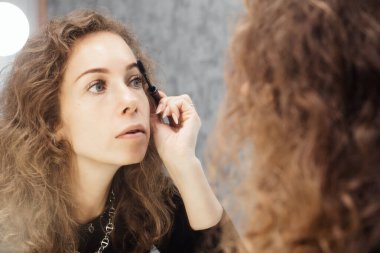 Güzel kız aynaya bakarken kaşları rötuş bir makyaj yapıyor.