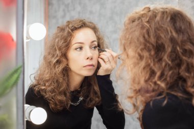 Güzel kız aynaya bakarken kaşları rötuş bir makyaj yapıyor.