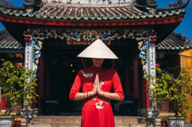 Asya 'daki bir Budist tapınağının arka planında koni şeklinde şapkalı ve geleneksel Vietnamlı elbiseli bir kadın..