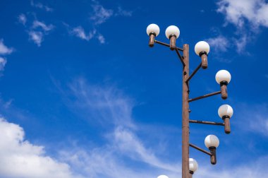 Çok sayıda küre ile süslenmiş şık bir sokak lambası canlı, bulutlu bir gökyüzüne karşı duruyor.