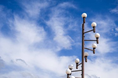 Çok sayıda küre ile süslenmiş şık bir sokak lambası canlı, bulutlu bir gökyüzüne karşı duruyor.