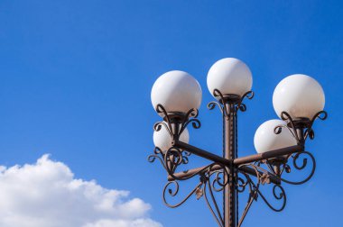 Açık mavi gökyüzünün altında beyaz küreleri olan klasik bir sokak lambası, herhangi bir şehir manzarasına cazibe katıyor..