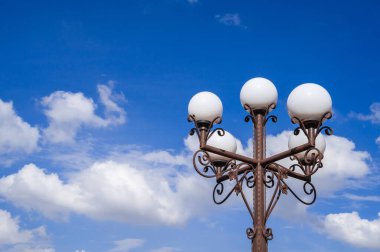 Açık mavi gökyüzünün altında beyaz küreleri olan klasik bir sokak lambası, herhangi bir şehir manzarasına cazibe katıyor.