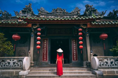 Geleneksel Vietnam kostümlü bir kadın, elinde vantilatör olan konik bir şapka Hoi An 'daki eski bir binanın arka planında. Tet bayramı ve yeni yıl