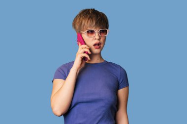 Beyaz bir kadın mavi arka planda cep telefonuyla konuşuyor. Teknoloji kavramı