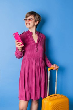 Sarı valizli mutlu kadın yaz tatilinde parlak mavi arka planda. Tatil kavramı.