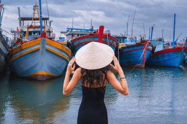 Geleneksel Vietnam şapkası takan bir kadın gezgin Da Nang limanında geleneksel ahşap tekneleri teftiş eder.
