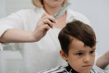Bir kadın kuaför, küçük bir çocuğun saçını makasla keser. Modern bir berber dükkanında profesyonel bir kuaför ve bir çocuk müşterisi..