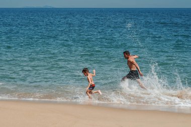 Baba ve oğul deniz kıyısında oynuyorlar. Baba ve bebek kumda koşuyorlar. Arkadaş canlısı aile kavramı..