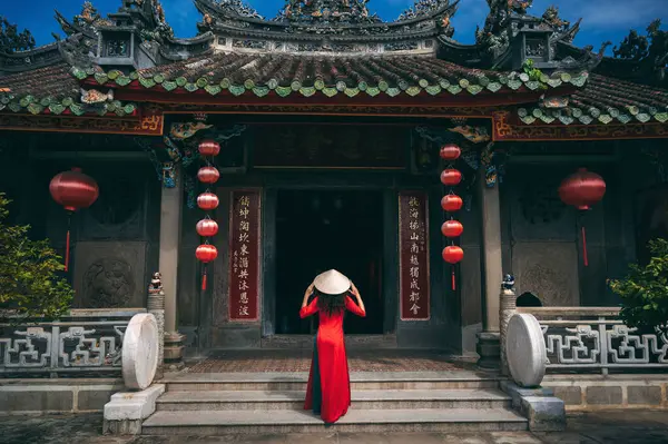 Vietnam 'da Hoi An' da eski bir binanın arka planında geleneksel bir Vietnam kostümü ve konik şapkası olan bir kadın.