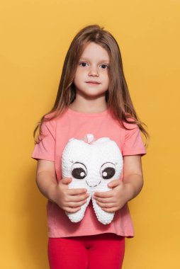 Sağlıklı dişleri olan gülümseyen bir kız sarı izole edilmiş bir arka planda oyuncak diş tutuyor. Mesajın için bir yer. Ağız temizliği. Pediatrik dişçilik. Protezler. Diş fırçalama kuralları. Dikey fotoğraf.