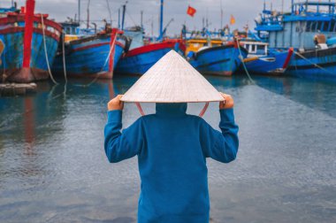 Geleneksel Vietnam şapkalı bir çocuk gezgin Da Nang limanında geleneksel ahşap tekneleri teftiş ediyor.