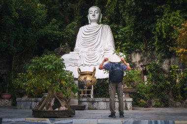 Vietnam şapkalı bir erkek gezgin Da Nang 'daki Mermer Dağlar' daki beyaz mermer Buda heykelinin önünde.