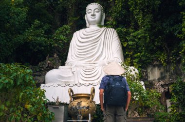 Vietnam şapkalı bir erkek gezgin Da Nang 'daki Mermer Dağlar' daki beyaz mermer Buda heykelinin önünde.