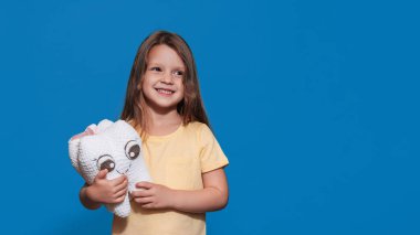 Sağlıklı dişleri olan gülümseyen bir kız mavi izole bir arka planda elinde bir diş oyuncağı tutuyor. Mesajın için bir yer. Ağız temizliği. Pediatrik dişçilik. Protezler. Diş fırçalama kuralları