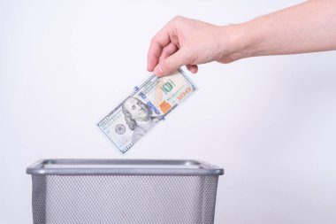 Bir el, dolar banknotlarını gri bir arka plana fırlatıyor. Gereksiz para birimi kavramı.