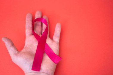 Kırmızı arka planda AIDS hakkında kırmızı kurdele tutan bir el. 1 Aralık 'taki Dünya AIDS Günü konsepti.