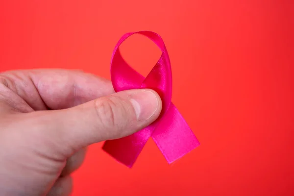 AID red ribbon in hand on red background symbolizing the fight against HIV, AIDS and cancer.