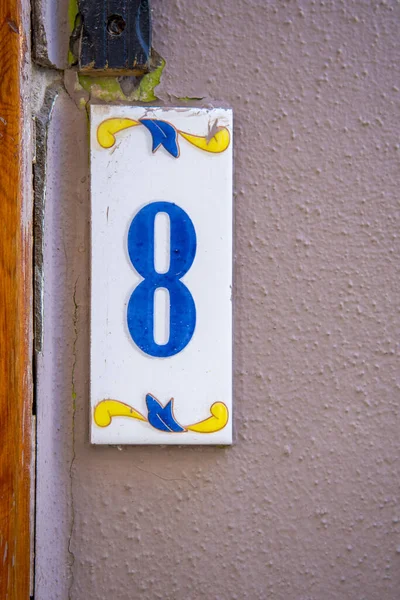A sign with the number 8 in blue on a pink wall. The concept of architecture and construction.