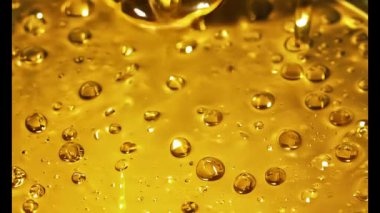 Bu büyüleyici görsel deneyimde, kalın bir altın sıvı zarifçe alçalıyor, aşağıdaki parıldayan yüzeyde dalgalanmalar ve yansımalar yaratıyor..