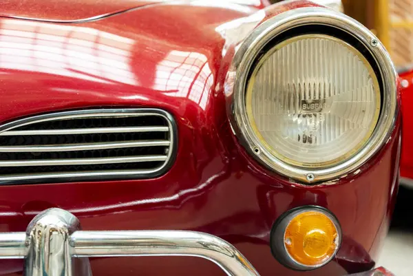 Parlak kırmızı klasik araba farları bir müzenin içini aydınlatıyor, geçmişten kalma klasik otomobillerin işçiliğini ve tasarımını vurguluyor..