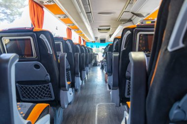 Modern bir otobüsün içi sıra sıra dizilmiş geniş koltukları sergiliyor. Güneş ışığı pencerelerden süzülüp konforlu koltuklara vurgu yapıyor. Ortam rahatlatıcı ve rahatlatıcı..
