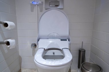 Zarif, gelişmiş bir tuvalet, pürüzsüz beyaz fayanslar ve paslanmaz çelik atık kutusuyla el değmemiş bir tuvalette bulunuyor. Doku ruloları kullanıcı rahatlığı için yakına yerleştirilir.