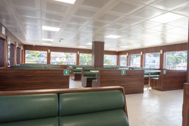 Feribottaki parlak ve geniş oturma yerleri, yeşil banklar, ahşap duvarlar ve kıyı kasabası manzaralı geniş pencereleri gösteriyor, huzurlu bir atmosfer sunuyor..