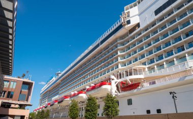 Lüks bir yolcu gemisi, güneşli bir günde parlak mavi gökyüzüne karşı zarif tasarımını ve cankurtaran botlarını sergileyerek yoğun bir rıhtıma demirlemiştir..