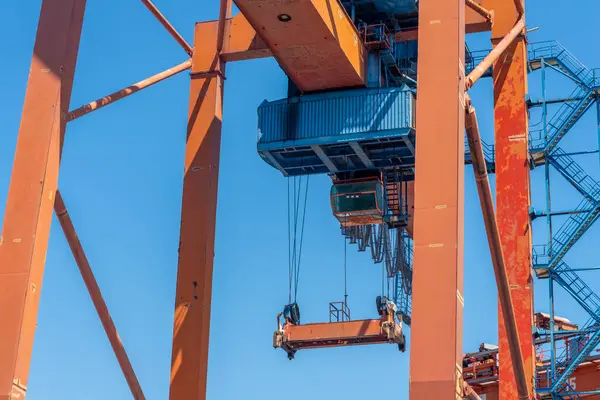 Açık mavi gökyüzüne karşı parlak turuncu yapısı ile bir liman ayarında büyük bir vinç kuleleri.