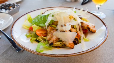 Lezzetli bir ızgara tavuk salatasında taze tavuk parçaları, taze sebzeler ve gün ortasında canlı bir restoranda servis edilen tıraş edilmiş peynir yer alıyor. Serinletici bir içecek yemeği tamamlar..