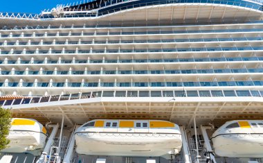 Pürüzsüz tasarımını sergileyen büyük bir yolcu gemisi limana yanaştı. Filikalar yapının altında görülebilir, güvenlik özelliklerini vurguluyorlar.