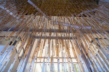 Karmaşık bir tasarım, tavandan sarkan sayısız ahşap çubuğu sergiliyor ve gölgelik etkisi yaratıyor. Doğal ışık, sanatsal ortamı geliştirmek için filtreler..