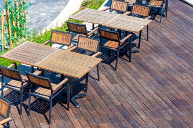 Ahşap masa ve sandalyelerin bir koleksiyonu şık bir verandada titizlikle düzenlenir. Güneşli öğleden sonra modern tasarımı vurguluyor. Rahatlamak için davetkar atmosferi arttırıyor..