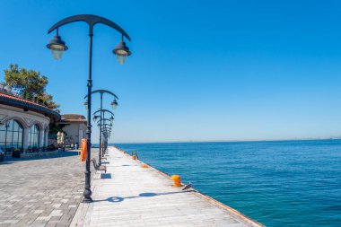 Huzurlu bir rıhtım rıhtımı berrak mavi sulara uzanıyor, parlak bir gökyüzünün altında uzun lambalarla kaplı..
