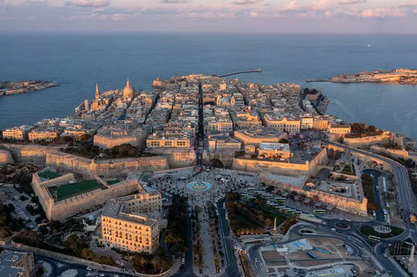 Gün batımında Valletta, Malta 'nın havadan görünüşü simetrik şebeke düzeni, tarihi kireçtaşı binalar, güçlendirilmiş duvarlar ve Akdeniz' e tepeden bakan Carmel Dağı 'nın Bazilikası' nın ikonik kubbesi..