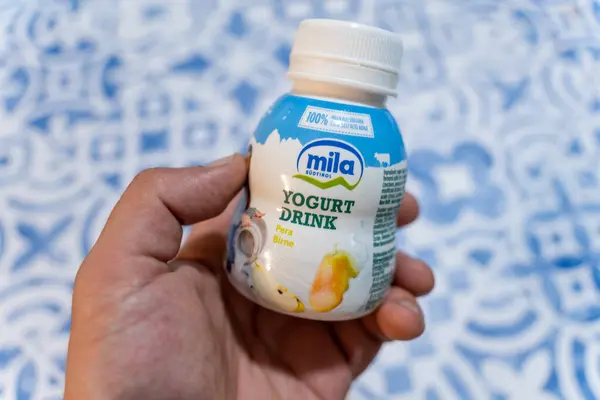 Bir şişe Mila Sudtirol armut aromalı yoğurt ile desenli bir arka plana karşı el ele tutuşmak