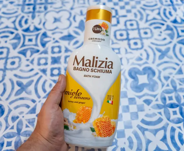 Mavi desenli bir yüzeyde bir şişe Malizia Bal ve Zencefilli Banyo Köpüğü