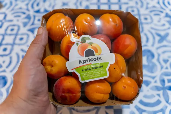 Bir tepsi taze kayısıyı mavi ve beyaz desenli masa örtüsünün üstünde tutarak.