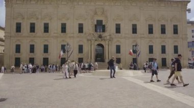 Turist grupları Valletta, Malta 'daki Auberge de Castille' in dışında toplanıyor. Barok simgesi, şimdi Başbakanlık Ofisi, süslü bir taş cephesi ve tarihi mimari barındırıyor..