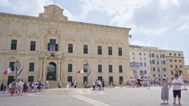Turist grupları Valletta, Malta 'daki Auberge de Castille' in dışında toplanıyor. Barok simgesi, şimdi Başbakanlık Ofisi, süslü bir taş cephesi ve tarihi mimari barındırıyor..