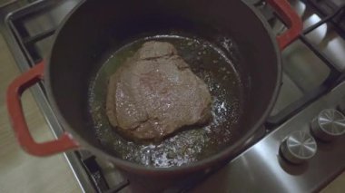 Kırmızı dökme demir tavada pişen lezzetli bir bifteğin yakın plan çekimi.