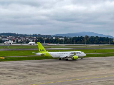 new Air Baltic airplane Airbus A220-300, registration  YL-ABT, taxiing on runway ready for departure on a cloudy day, two aircrafts of Swiss Airlines in background at International Airport Zurich, Switzerland,100624  clipart