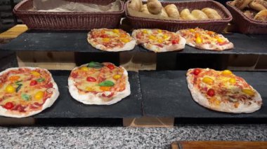 Pizzalar, domatesler, fesleğenler ve Mozzarella peynirleri restoranda sergilenmekte olan siyah taş tabaklar, sepetlerde ekmek çörekleri.